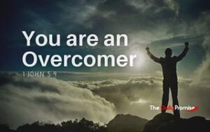 Man standing on a mountain with his hands raised. "You are an overcomer" 1 John 5:4