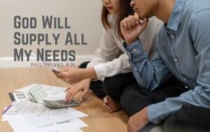 A couple sitting on the floor reniewing their bills - "God Will Supply All My Needs." Philippians 4:19