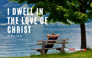 A man is leaning back on a bench that is sitting at the edge of a lake. His hands are resting above his head. "I Dwell in the Love of Christ" - John 15:9