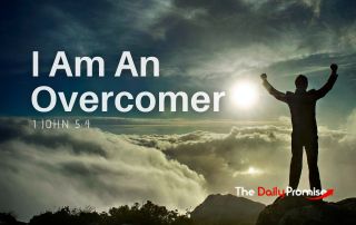 A man standing on a mountain with his hands raised. "I Am An Overcomer". 1 John 5:4