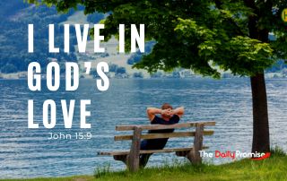 A man is leaning back on a bench that is sitting at the edge of a lake. His hands are resting above his head. "I Live in God's Love" - John 15:9