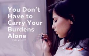 A woman is looking out a window with a worried look on her face. Beside her are the words, “You Don't Have to Carry Your Burdens Alone” – Psalm 55:22